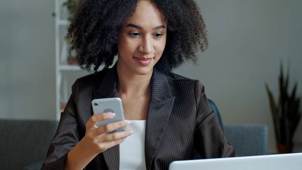 African american businesswoman freelancer student girl woman sit at home office read sms email on mobile phone work online by computer develop business project distant education use modern technology - 写真・画像