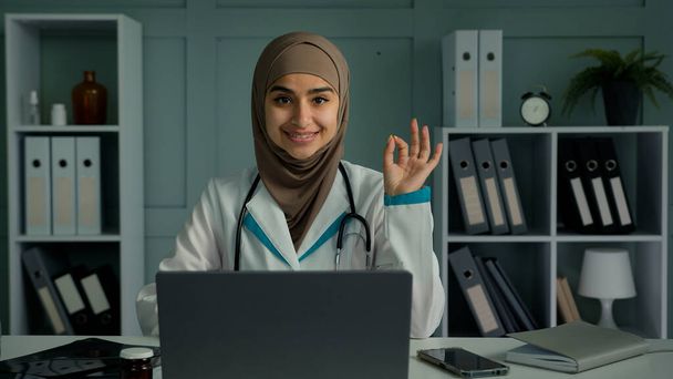 Iloinen onnellinen arabian Lähi-idän lääkäri nuori islamilainen uskonto nainen harjoittaja terapeutti kardiologi hammaslääkäri lääkäri valkoisessa takissa suositella hyvää terveydenhuoltopalvelua tehdä ok käsi ele - Valokuva, kuva