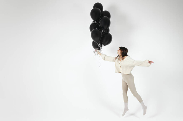 Brunette Girl in light clothes jumping with Bunch of black balloons. Isolated on white background. - Fotografie, Obrázek