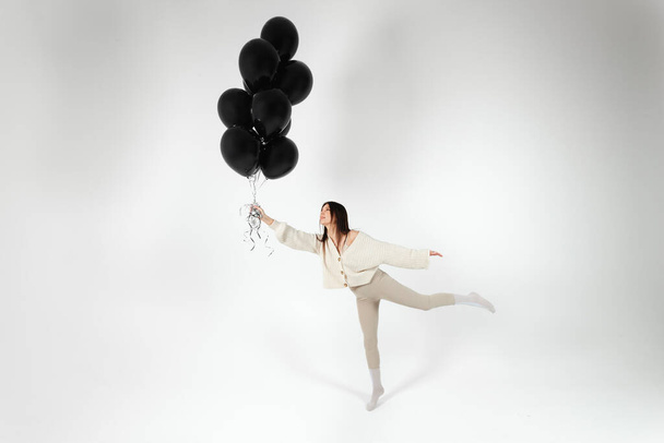 Brünettes Mädchen in leichter Kleidung springt mit einem Bündel schwarzer Luftballons. Isoliert auf weißem Hintergrund. - Foto, Bild