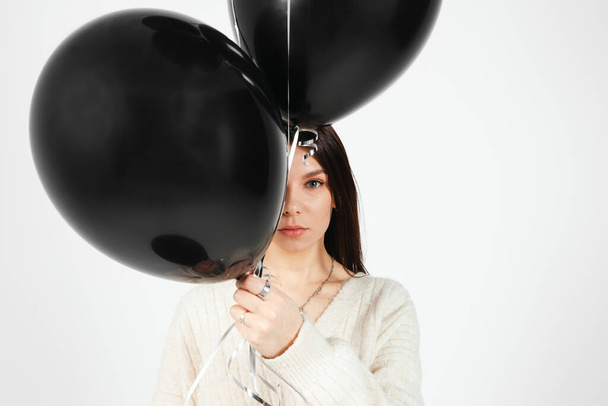 Portrait of Young brunette holding bunch of black balloons, isolated on white background. - Photo, image
