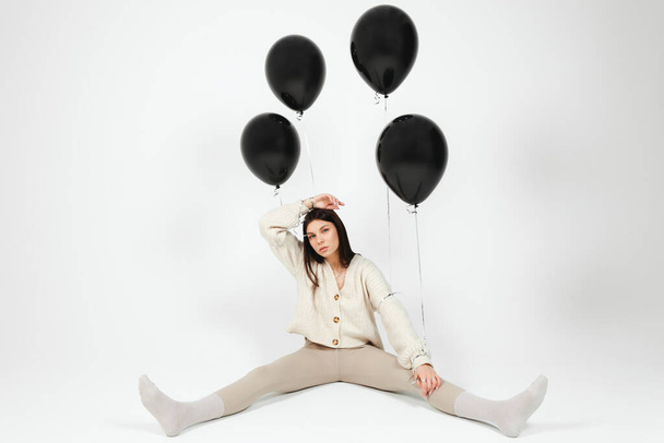 Young brunette in light clothes holding bunch of black balloons, isolated on white background. - Фото, изображение