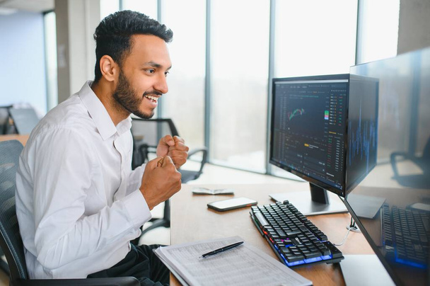 Portrait of a positive successful Indian or Arabian trader, stock market broker, Crypto charts on laptop screen. - Photo, image