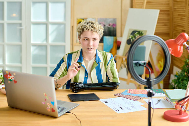 Joven blogger confiada dando clase magistral o entrenamiento a la audiencia en línea mientras está sentada frente a la cámara del teléfono inteligente en casa - Foto, imagen