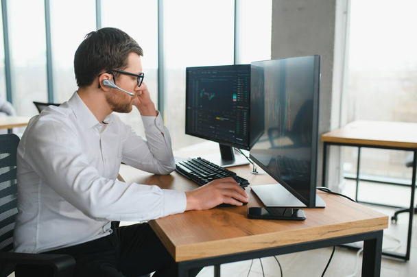 Man trader in formalwear sitting at desk in frot of monitors with charts and data at office - Photo, image