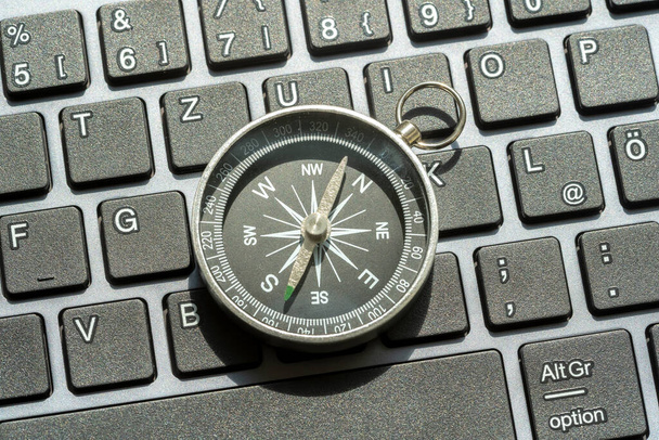Jeden kompas ležící na moderní počítačové klávesnici PC, světová navigace, různé směry, NSWE objekt detailní up, nikdo, centrální kompozice, technologie. Výběr trasy, koncept cesty - Fotografie, Obrázek