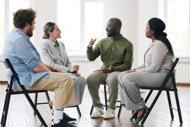 Nuori musta mies selittää jotain hän on huolissaan naispuoliselle psykoterapeutille ja rotujenvälinen potilaille, jotka osallistuvat psykologiseen istuntoon. - Valokuva, kuva