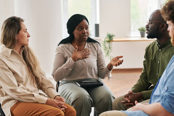 Donna di colore fiduciosa che descrive il suo problema mentale o preoccupazioni ad altre persone sedute intorno durante la sessione psicologica - Foto, immagini