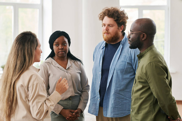 Group of young interracial people discussing their problems and giving advice to one another while attending course of psychological help - 写真・画像
