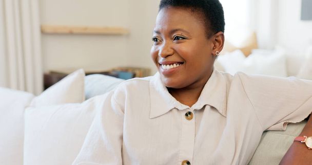 Szczęśliwa, uśmiechnięta i czarna kobieta relaksująca się na kanapie podczas oglądania telewizji w salonie swojego nowoczesnego domu. Szczęście, śmiech i afrykańska dama streamująca film siedząc na kanapie w swoim salonie. - Zdjęcie, obraz
