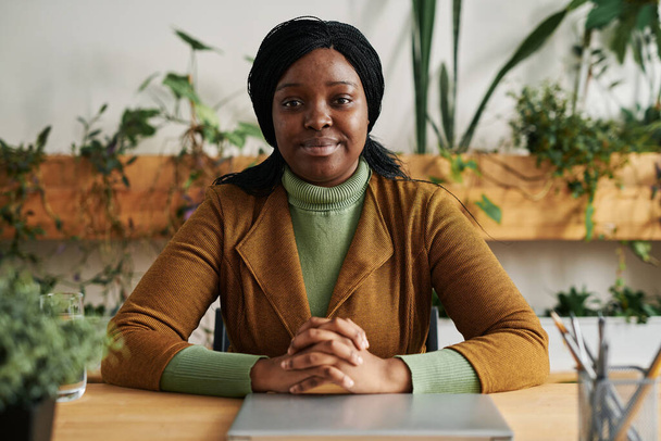 Νεαρή γυναίκα αφροαμερικανή ψυχολόγος με αυτοπεποίθηση σε smart casualwear που κάθεται στο γραφείο και κοιτάζει την κάμερα - Φωτογραφία, εικόνα