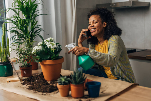Belle femme de race mixte heureux travaille avec des plantes et avoir une conversation au téléphone - Photo, image