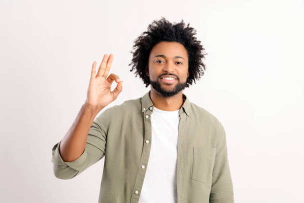 Charismatic cheerful curly african american man 30s showing Ok gesture in sign og approval and agreement standing isolated on white background, guy demonstrating that everything under control - Foto, afbeelding