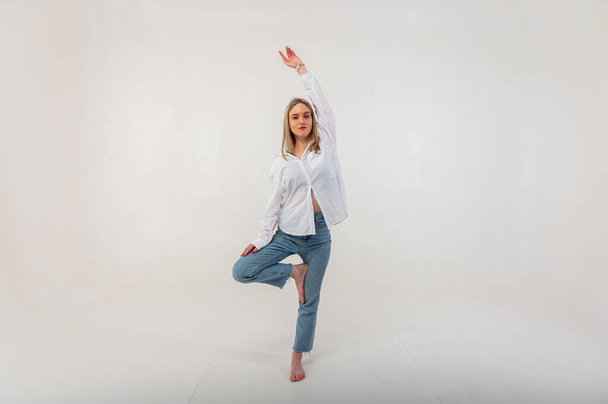 Sporty energetic active young girl stands on one leg meditating om sign, relaxes, rests. Light background with place for writing - Foto, Bild