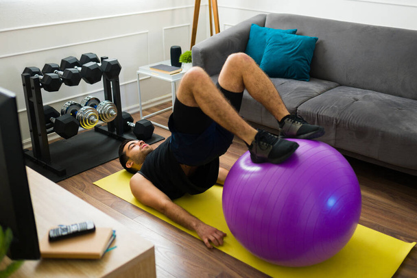 Active hispanic young man using a stability ball for his home workout exercises in the living room - Φωτογραφία, εικόνα