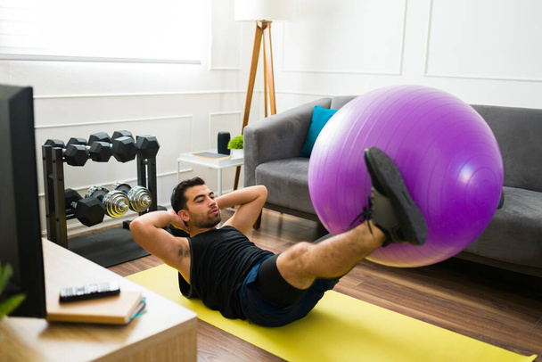 Sporty latin man in the living room doing abdominal crunches exercises using a stability ball - Foto, Imagem