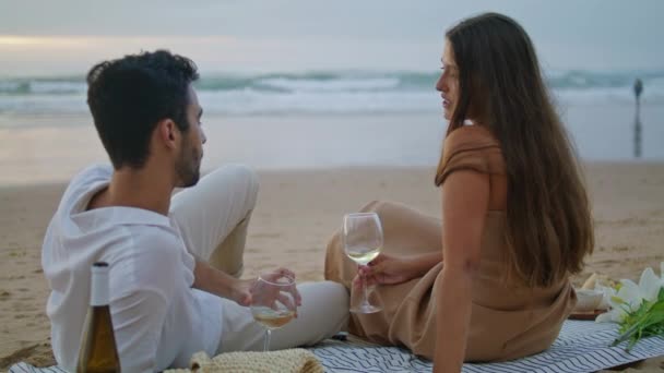 Sensual couple celebrating vacation at seashore. Romantic family clinking glasses at sandy beach picnic. Cute sweethearts drinking alcohol beverage back view. Spouses spending anniversary together - Felvétel, videó