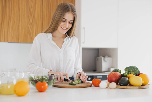 Una donna bionda carina sta preparando un'insalata in cucina - Foto, immagini