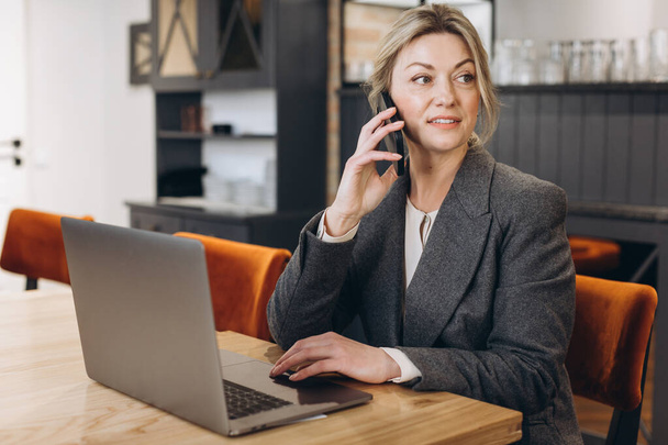Reife Geschäftsfrau Restaurantfachfrau sitzt am Telefon und arbeitet am Laptop - Foto, Bild