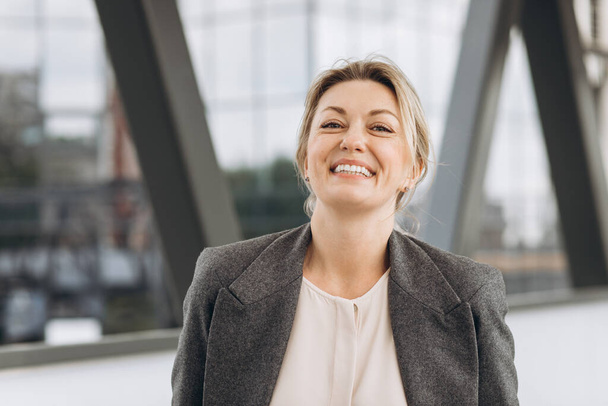 Portret van een volwassen zakenvrouw glimlachend met emoties op de moderne stedelijke en kantoorgebouwen achtergrond - Foto, afbeelding