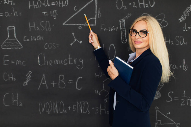 Portrait d'une enseignante blonde heureuse debout près du tableau noir dans la salle de classe. - Photo, image