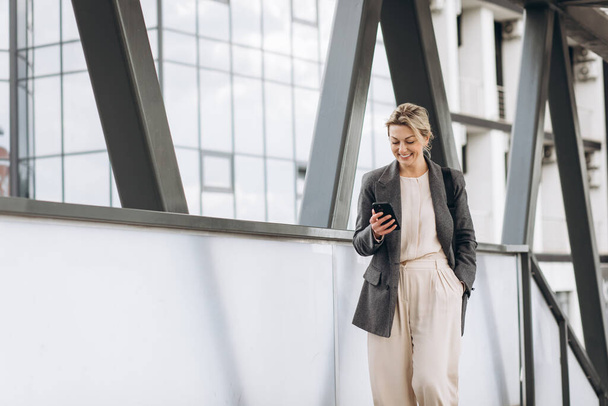 Portrait of a beautiful mature business woman in suit and gray jacket smiling and talking on the phone on the modern urban background - Foto, Bild