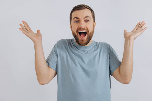 Portrait of a modern bearded middle-aged man in a blue t-shirt shows that he does not know emotion on a white background - Photo, Image