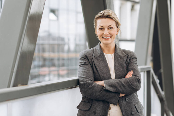 Porträt einer reifen Geschäftsfrau, die mit Emotionen über das moderne Büro und den urbanen Hintergrund lächelt - Foto, Bild