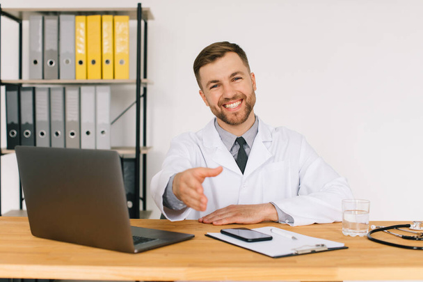 Glücklicher männlicher Arzt, der sich ein medizinisches Online-Webinar oder Schulungsseminar ansieht, während er am Arbeitsplatz mit seinem Laptop sitzt. - Foto, Bild