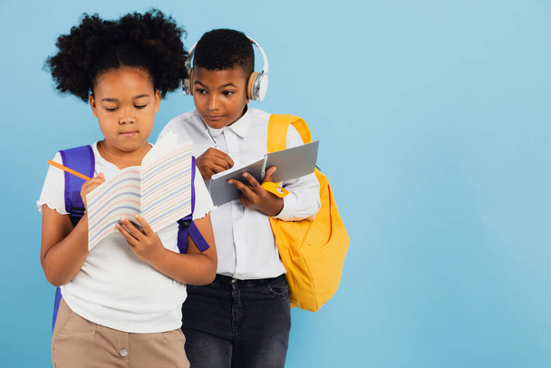 Mixed race schoolboy handing off homework to african american schoolgirl in school classroom on blue background, back to school concept. - Photo, Image