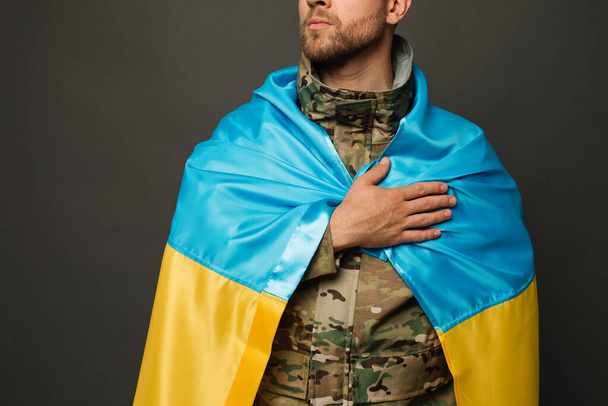Portrait of a courageous Ukrainian military man tied with the flag of Ukraine and holding hand on heart, freedom concept - Fotó, kép