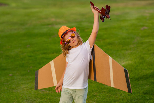 Boy kid dreams of becoming a pilot. Happy child playing outdoor. Kid having fun with toy paper wings - Foto, Imagen