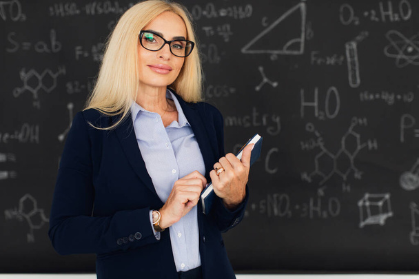 Портрет счастливой блондинки-учительницы, стоящей возле доски в классе. - Фото, изображение