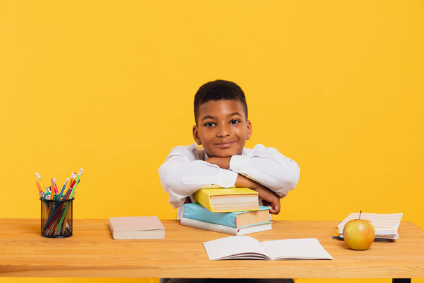 Щасливий африканський школяр сидить за столом, спираючись на книжки. Повернення до шкільної концепції. - Фото, зображення