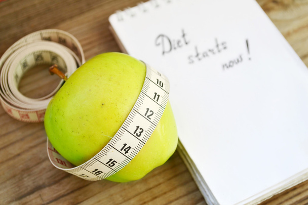 Concepto de dieta con manzana verde, un cuaderno y una cinta métrica en la mesa de madera
 - Foto, imagen