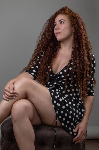 modelo feminino posando com pernas cruzou uma mulher latina com cabelos longos encaracolados em estúdio, beleza e moda - Foto, Imagem