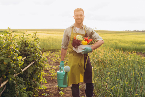 Щасливий фермер тримає кошик зі свіжими овочами та балончиками для поливу, концепція садівництва
 - Фото, зображення