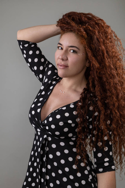 face of a beautiful latin woman playing with her long curly hair, beauty with natural makeup, young person portrait in studio - Fotó, kép