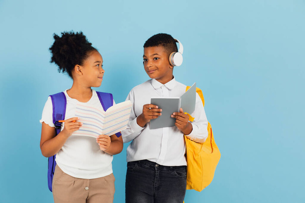 Afrikai iskolás fiú és afro-amerikai iskolás lány együtt olvassák az iskolai tanteremben a kék hátteret, vissza az iskolába koncepció. - Fotó, kép