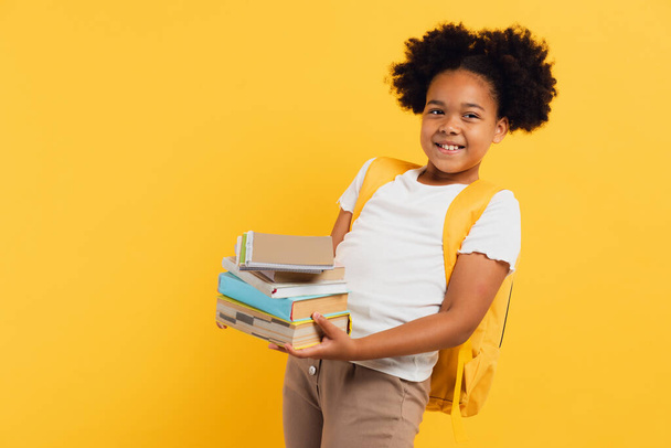Χαρούμενη Αφρο-Αμερικανίδα μαθήτρια που κρατάει σημειωματάρια και βιβλία σε κίτρινο φόντο, αντίγραφο χώρου. - Φωτογραφία, εικόνα