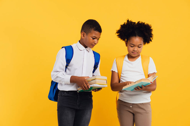 Boldog afro-amerikai iskolás lány és vegyes fajú iskolás fiú kezében könyvek sárga háttér, másolás tér. - Fotó, kép