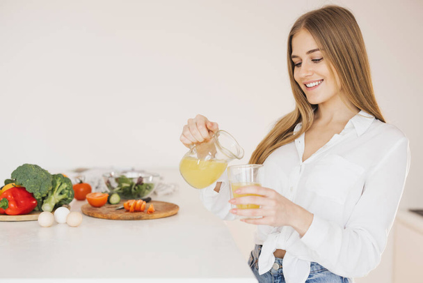 Une femme blonde mignonne heureuse boit du jus d'orange dans la cuisine - Photo, image