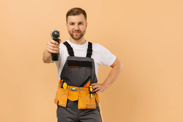 Positieve mannelijke reparateur thuis met schroevendraaier op beige achtergrond - Foto, afbeelding