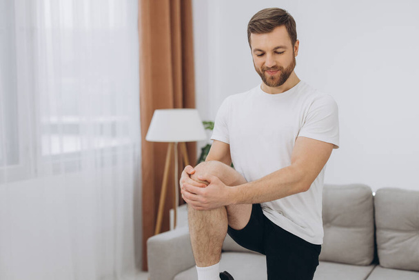 Handsome bearded man doing hamstring stretch exercise at home. - Photo, Image