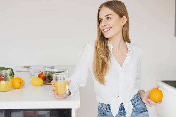 Cute blonde woman drinks orange juice in the kitchen - Foto, imagen