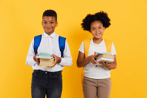 Mutlu Afro-Amerikan liseli kız ve karışık ırk öğrencileri ellerinde sarı arka plan üzerine kitaplar tutuyorlar.. - Fotoğraf, Görsel