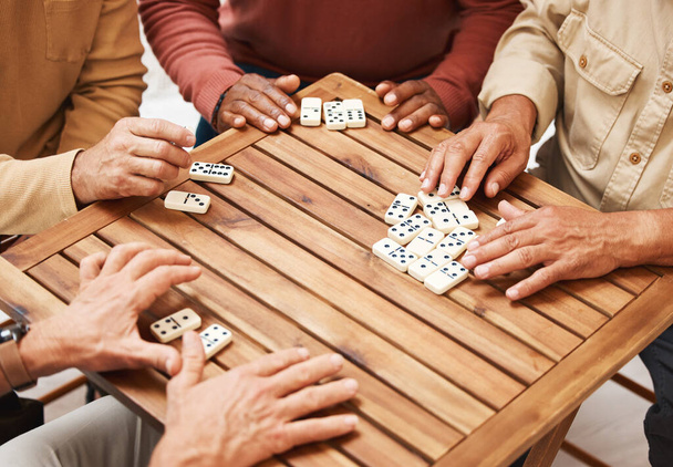 Hands, dominoes and friends in board games on wooden table for fun activity, social bonding or gathering. Hand of domino players with rectangle number blocks playing in group for entertainment. - Photo, image