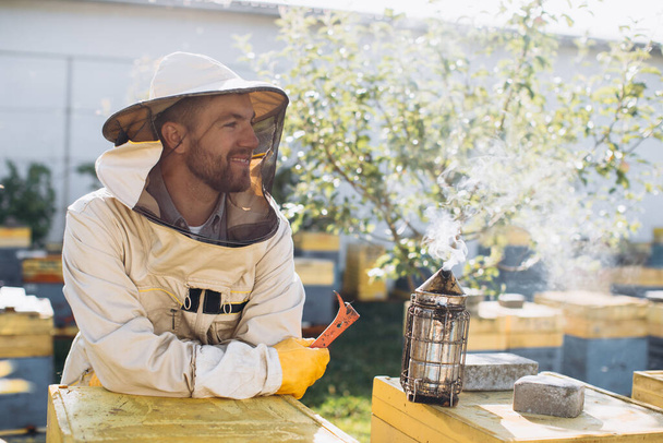 Portrait of a happy male beekeeper working in an apiary near beehives with bees. Collect honey. Beekeeper on apiary. Beekeeping concept. - Foto, immagini