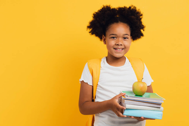 Not defterleri ve sarı arkaplan üzerine kitaplar tutan mutlu Afrikalı Amerikalı kız öğrenci, boşluğu kopyala. - Fotoğraf, Görsel