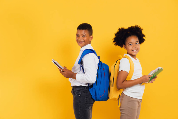 Onnellinen afrikkalainen koulutyttö ja koulupoika pitämässä kirjoja vierekkäin keltaisella pohjalla. Takaisin kouluun käsite. - Valokuva, kuva